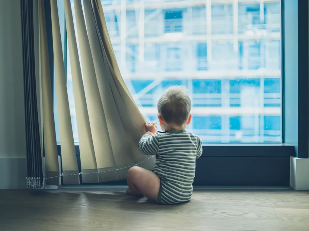 Little baby playing with blinds in an apartment