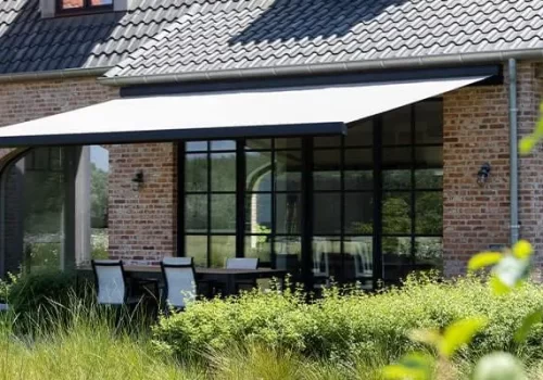 White retractable awning attached to a house proviing shade on glass doors and outdoor dining area